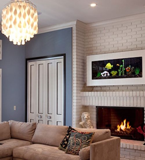 Aquarium with white frame and black background mounted above fireplace in home